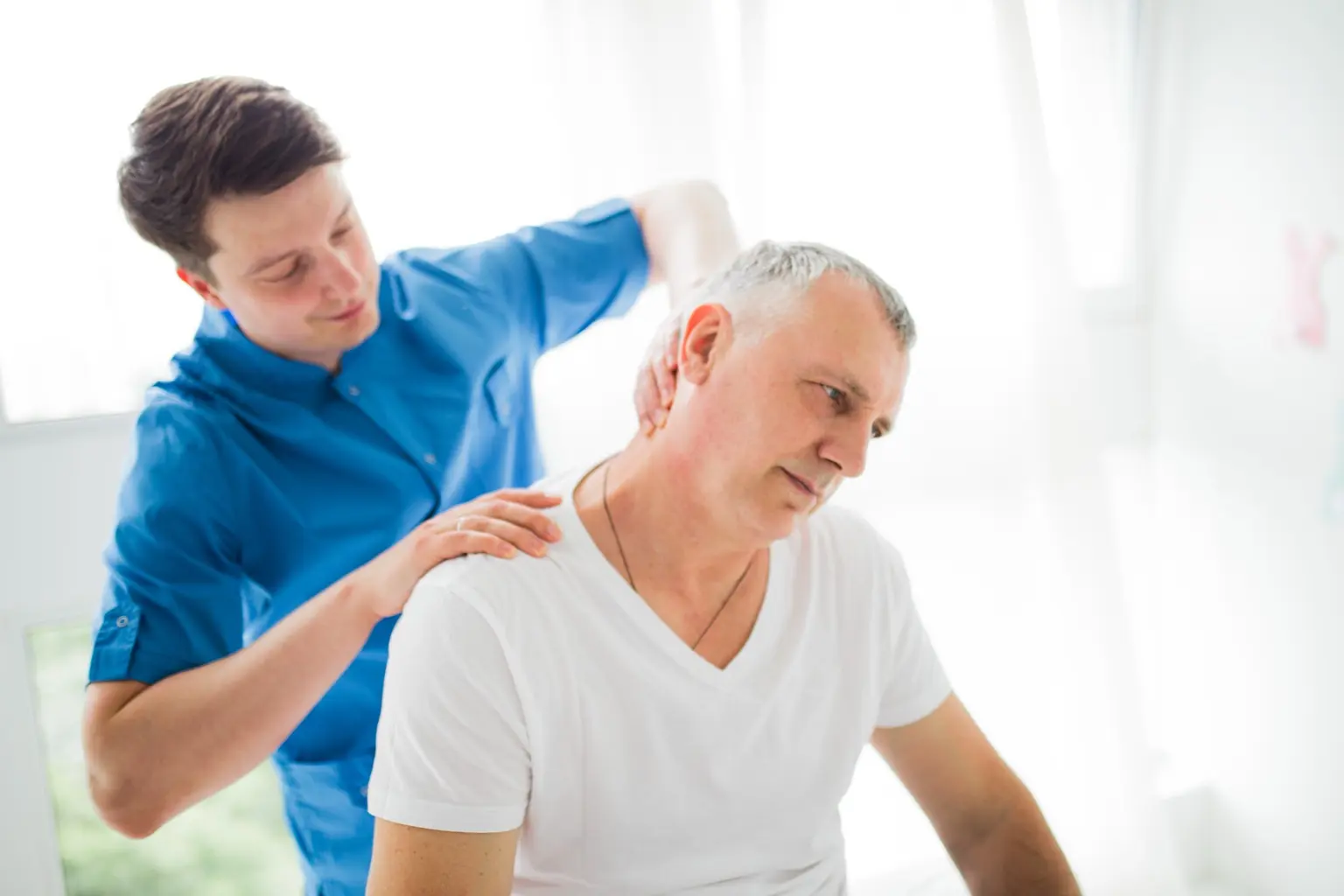 Massage therapist assessing and treating a seated client’s neck and shoulder movement